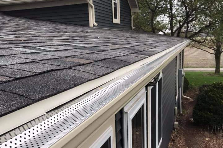 Close-up of asphalt shingle roof with aluminum gutter guard system installed along the roof edge.
