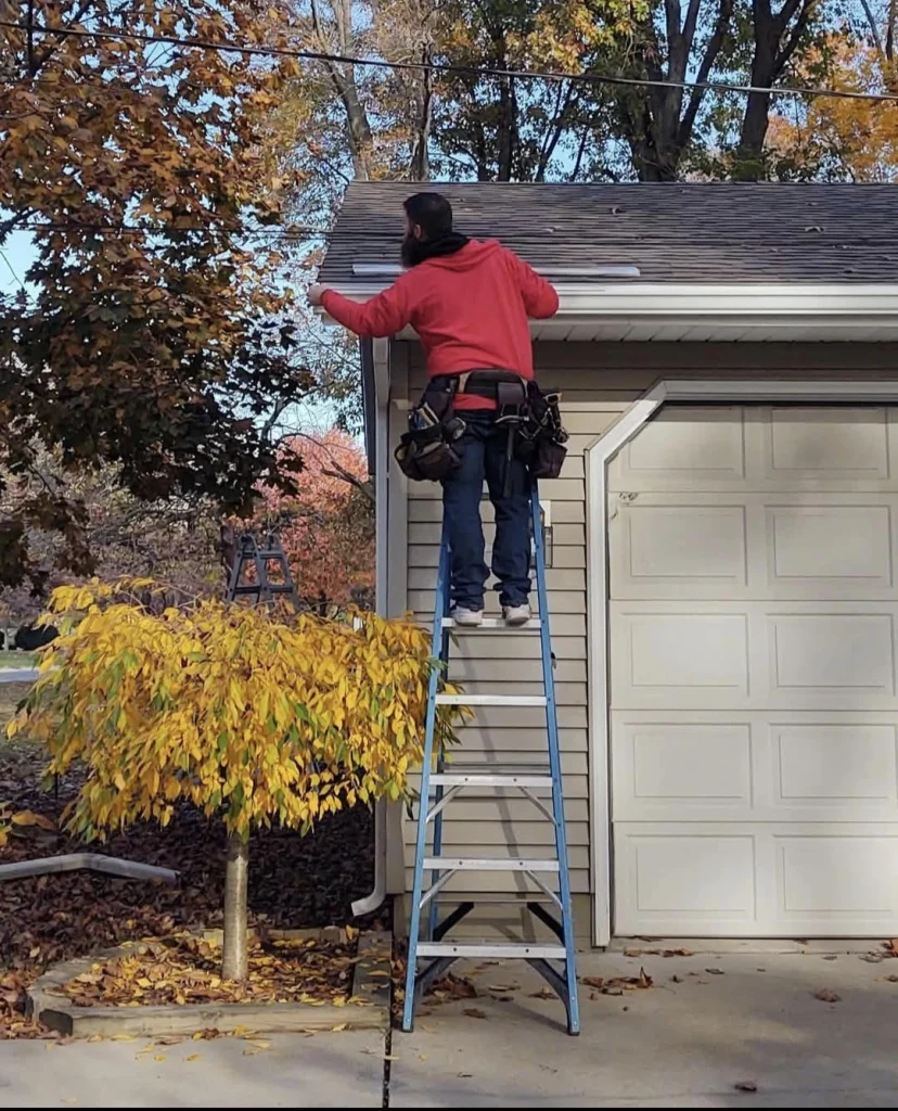 Contractor installing gutters on a residential home using a ladder during fall.
