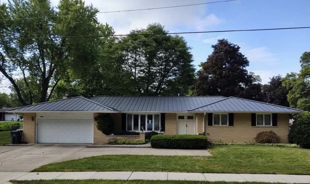 Single-story ranch home with a gray standing seam metal roof and attached garage in a residential neighborhood.